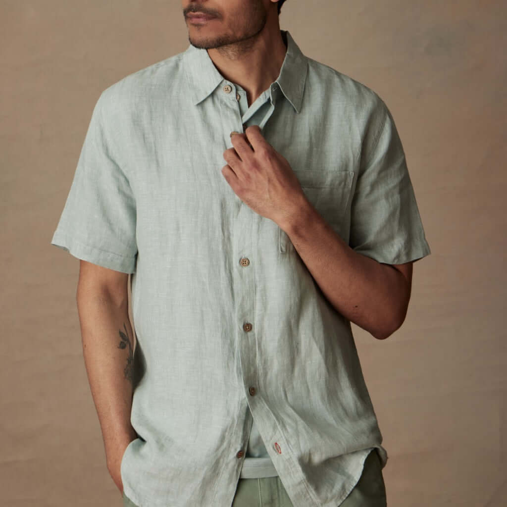 Model wearing a short sleeve teal mist linen shirt, featuring a spread collar and button closure, with a casual fit.