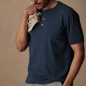 Model wearing a short sleeve melange henley shirt in deep cobalt, showcasing its classic design and 3-button placket.