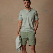 Man in short sleeve melange henley shirt in sea mist heather, paired with green shorts for a casual summer look.