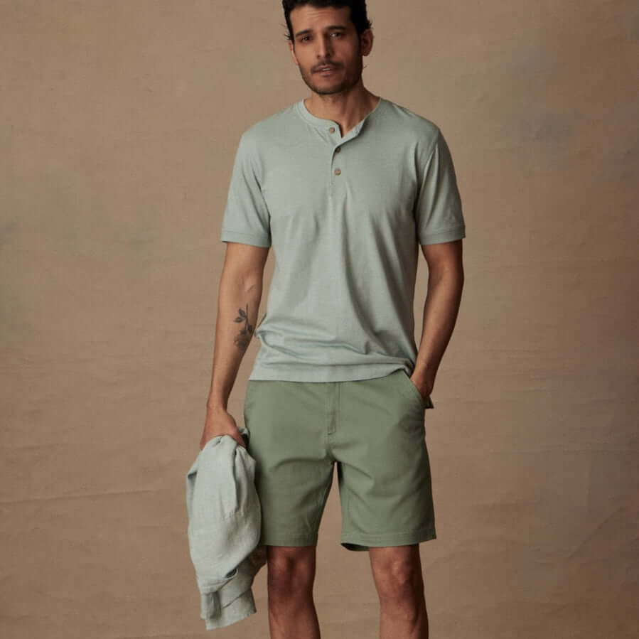 Man in short sleeve melange henley shirt in sea mist heather, paired with green shorts for a casual summer look.