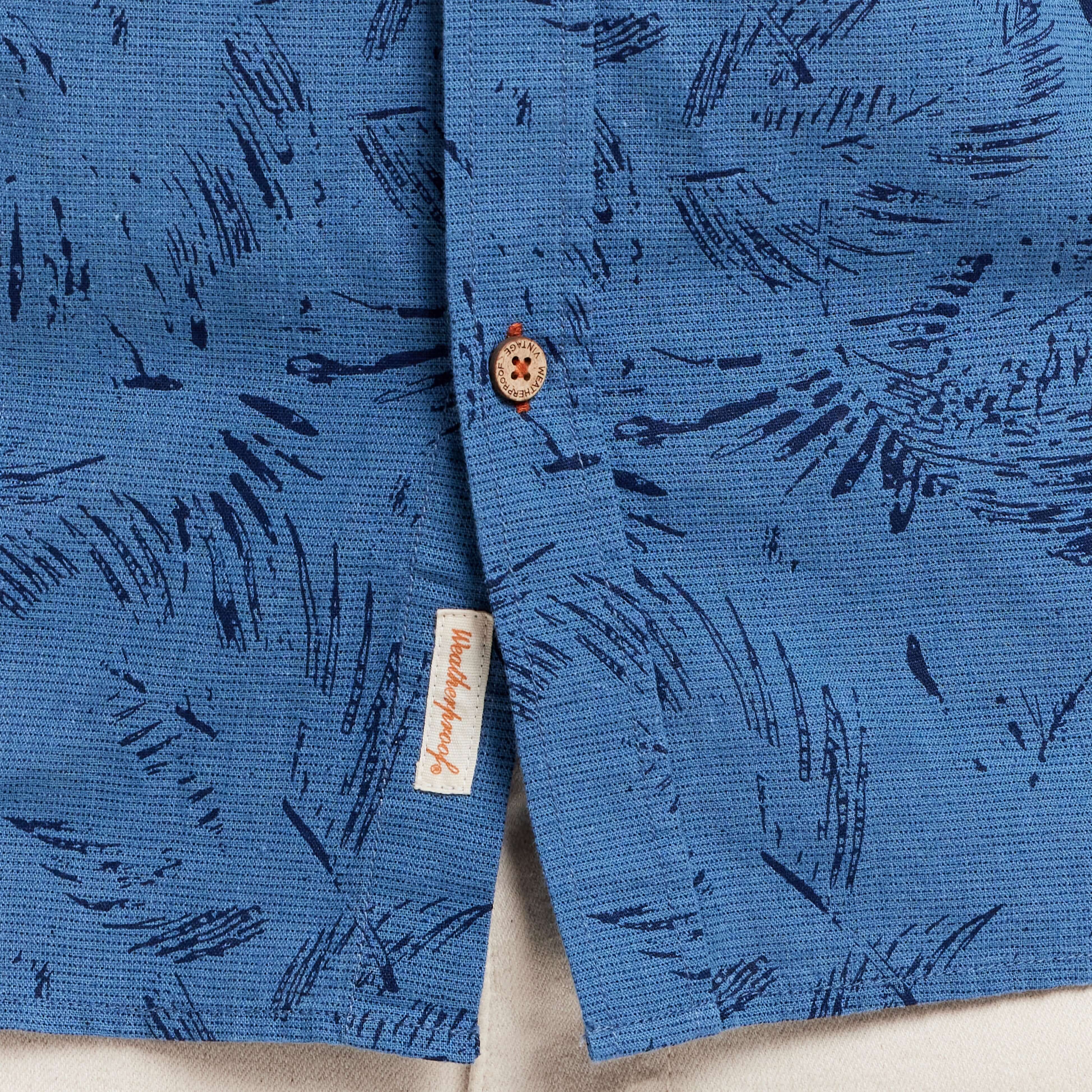 Close-up of a blue linen cotton shirt featuring abstract print and a button detail, showcasing relaxed fit and style.