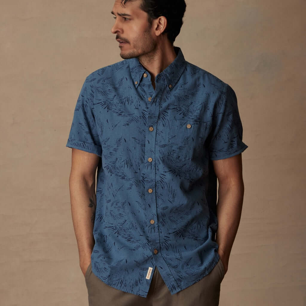 Model wearing a short sleeve blue ashes linen cotton shirt with abstract print, featuring button-down front and patch pocket.