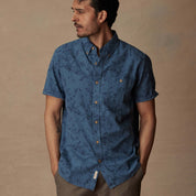 Model wearing a short sleeve blue ashes linen cotton shirt with abstract print, featuring button-down front and patch pocket.