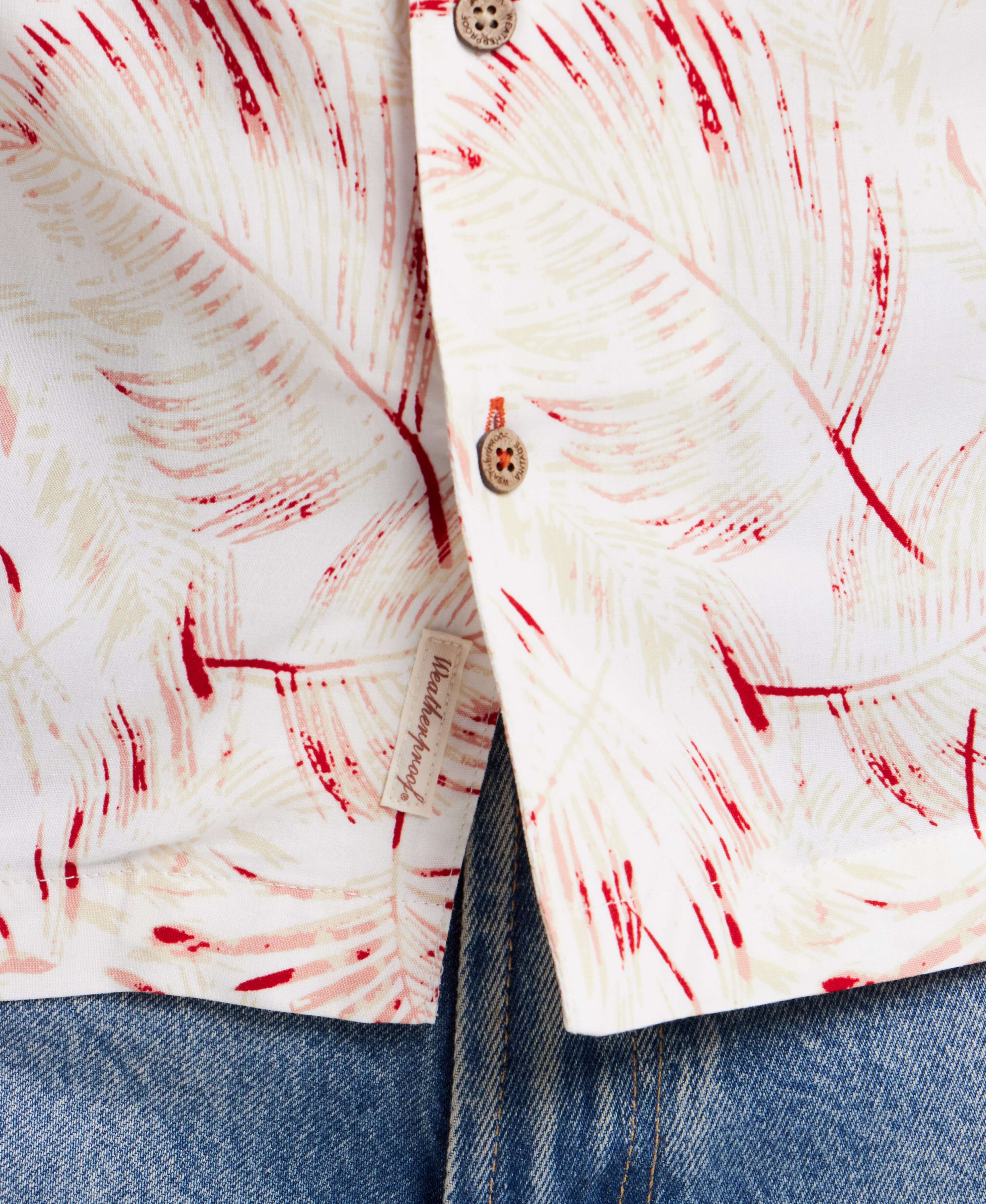 Short sleeve rayon camp shirt in dusty pink with a retro leaf pattern, paired with blue jeans, showcasing front buttons and pocket.