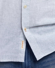 Close-up of a neatly buttoned light blue linen cotton shirt, featuring a stitched label and casual denim.