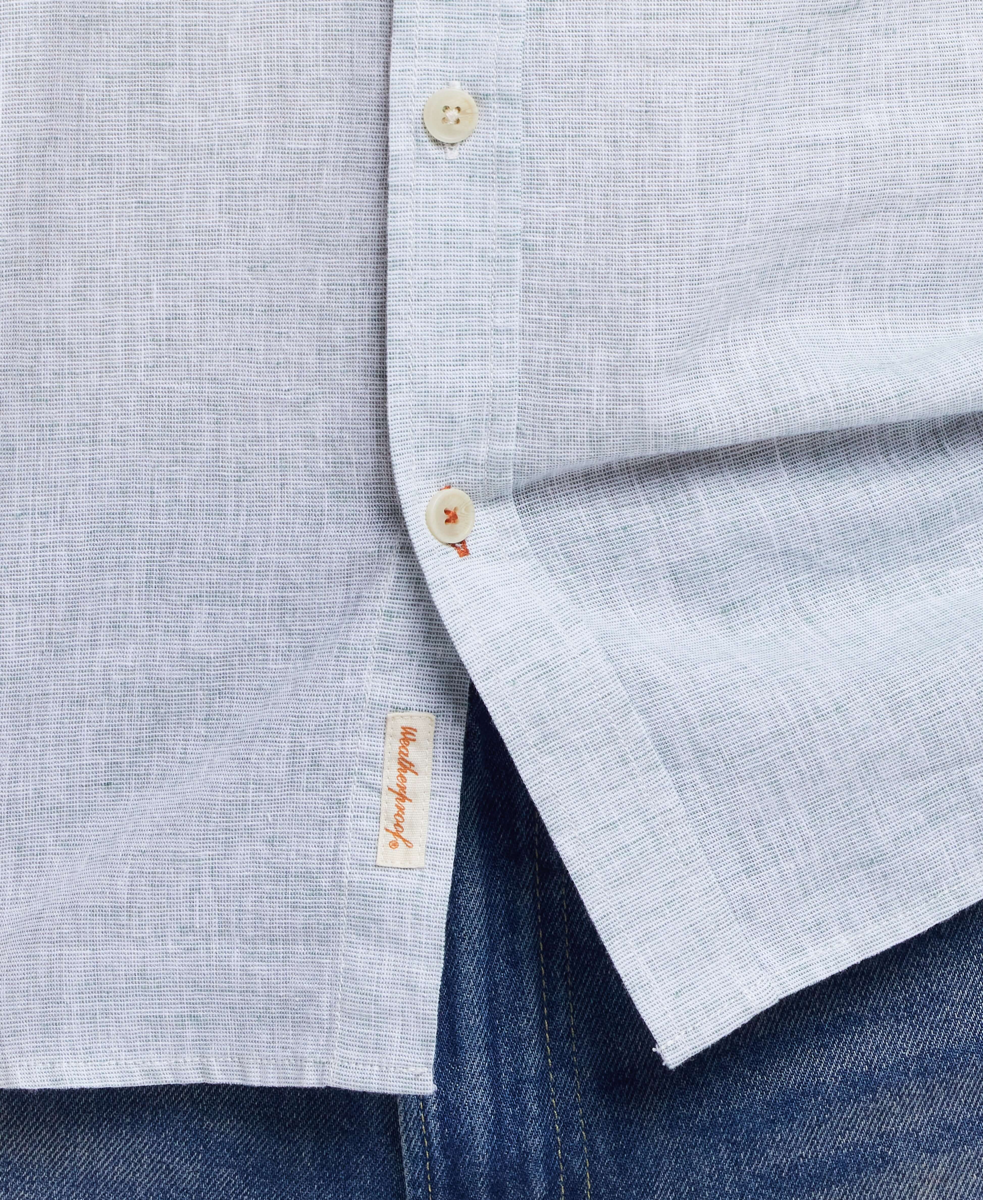Close-up of a neatly buttoned light blue linen cotton shirt, featuring a stitched label and casual denim.
