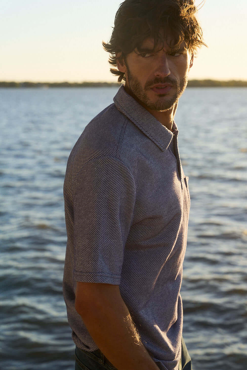 Man wearing a peacoat navy short sleeve twill polo shirt by the water in natural light.
