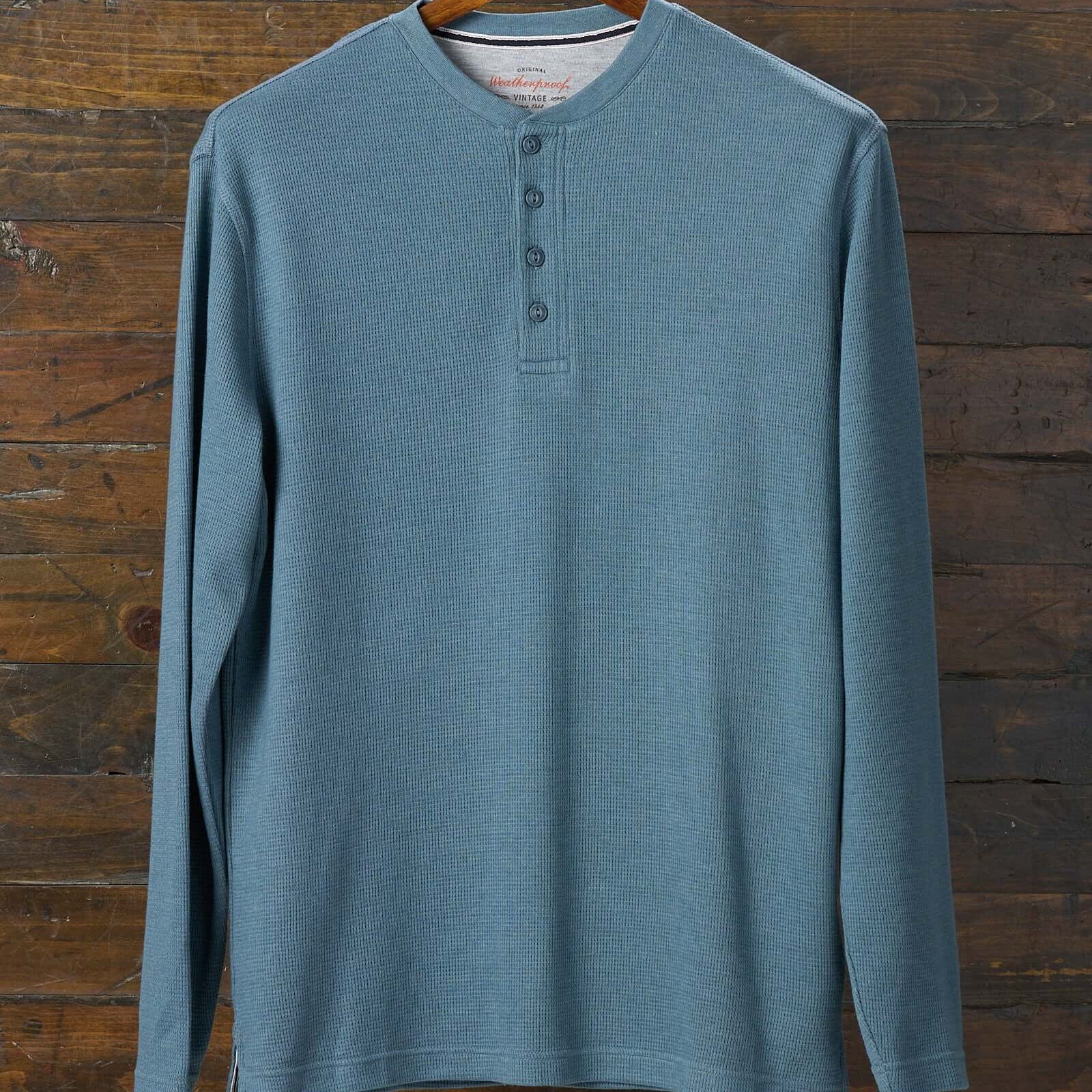 Long Sleeve Waffle Henley in Storm Blue displayed on a wooden hanger against a rustic backdrop.