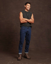 Confident man wearing slim fit denim jeans in Carolina blue, styled with a sleeveless shirt and rugged boots.