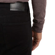 Close-up of a man's hand on the back pocket of slim fit jet black denim jeans, showcasing quality stitching and detail.