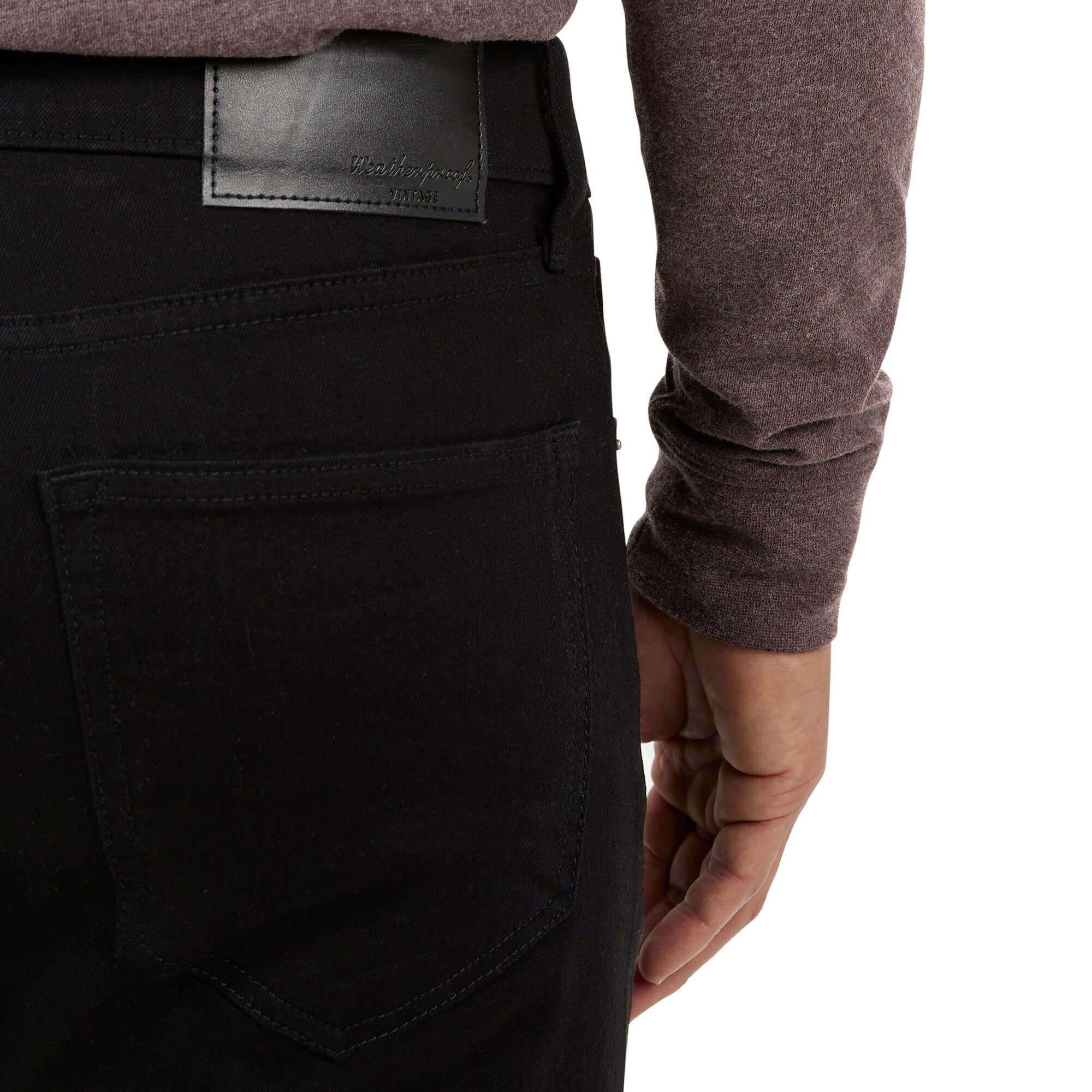Close-up of a man's hand on the back pocket of slim fit jet black denim jeans, showcasing quality stitching and detail.