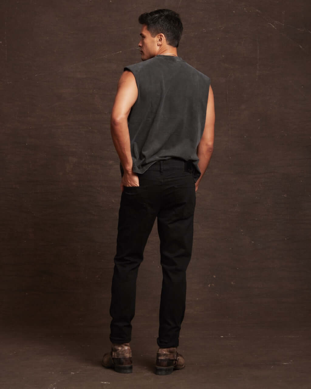 Model showcasing slim fit denim jeans in jet black from the back, paired with a sleeveless top and boots.