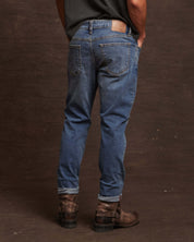 Man showcasing slim fit denim jeans in Rocker Blue, featuring a comfortable all-way stretch and stylish cuffed hem.