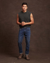 Man wearing slim fit denim jeans in soft blue, styled with a sleeveless black top and brown boots.