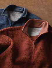 Teddy sherpa pullover quarter-zips in Pageant Blue and a warm rust color, showcasing soft fleece texture and cozy design.
