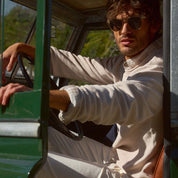Man in sunglasses wearing a Twill Stonewash Sweater in Natural, seated in a vintage vehicle, embodying casual style.