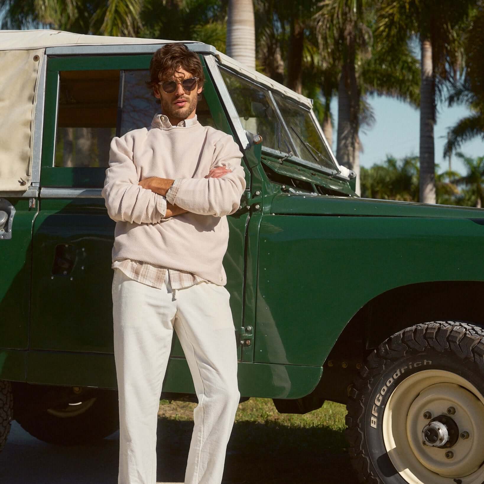 Stylish man in a natural twill stonewash sweater, standing next to a vintage green vehicle, exuding effortless casual cool.