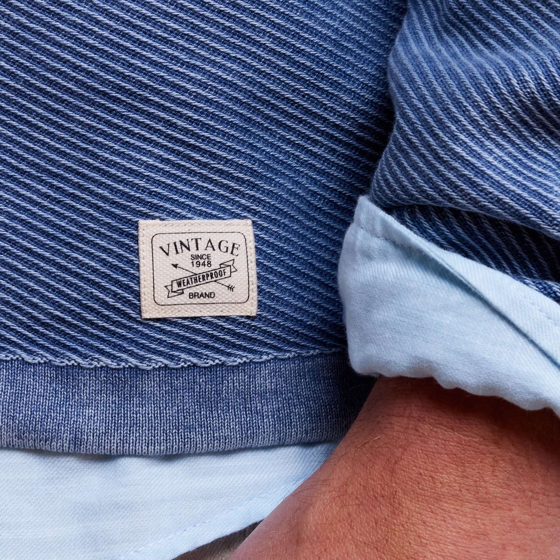 Vintage label on a blue stonewash sweater showcasing textured knit detail and a timeless fashion statement.