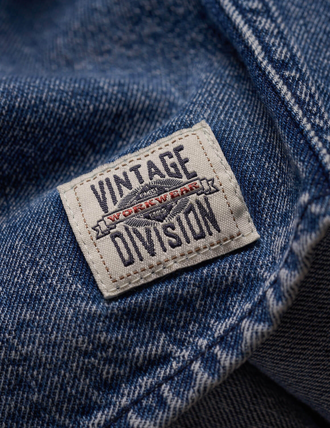 Close-up of the tag on a Denim Shirt In Acid Blue, featuring the Vintage Division logo on soft, faded fabric.