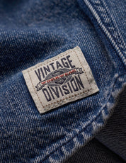 Close-up of the tag on a Denim Shirt In Acid Blue, featuring the Vintage Division logo on soft, faded fabric.