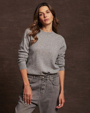 Woman wearing a medium grey cashmere long sleeve crew sweater, styled with relaxed jeans.