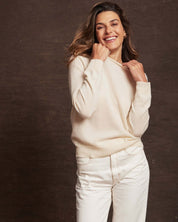 Woman in ecru cashmere long sleeve sweater with ribbed cuffs, smiling against a brown backdrop.