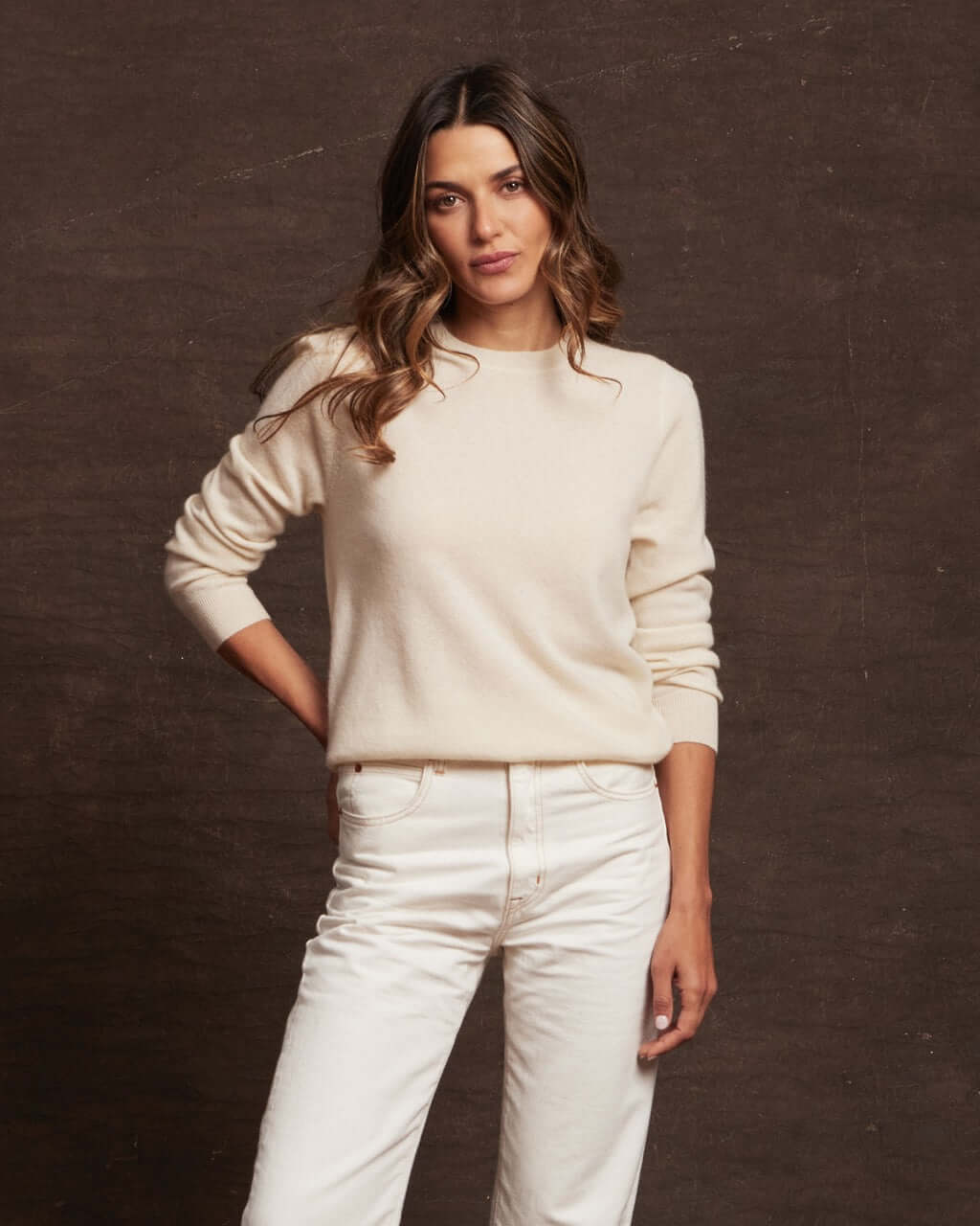 A woman wearing a women's ecru cashmere long sleeve crew sweater, styled with white jeans for a chic winter look.
