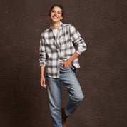 Smiling woman wearing a blue checkered women's stretch flannel shirt with rolled sleeves and relaxed jeans.