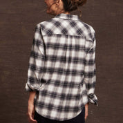 Back view of a woman wearing a black and white plaid women's stretch flannel shirt, showcasing its classic fit and rolled sleeves.