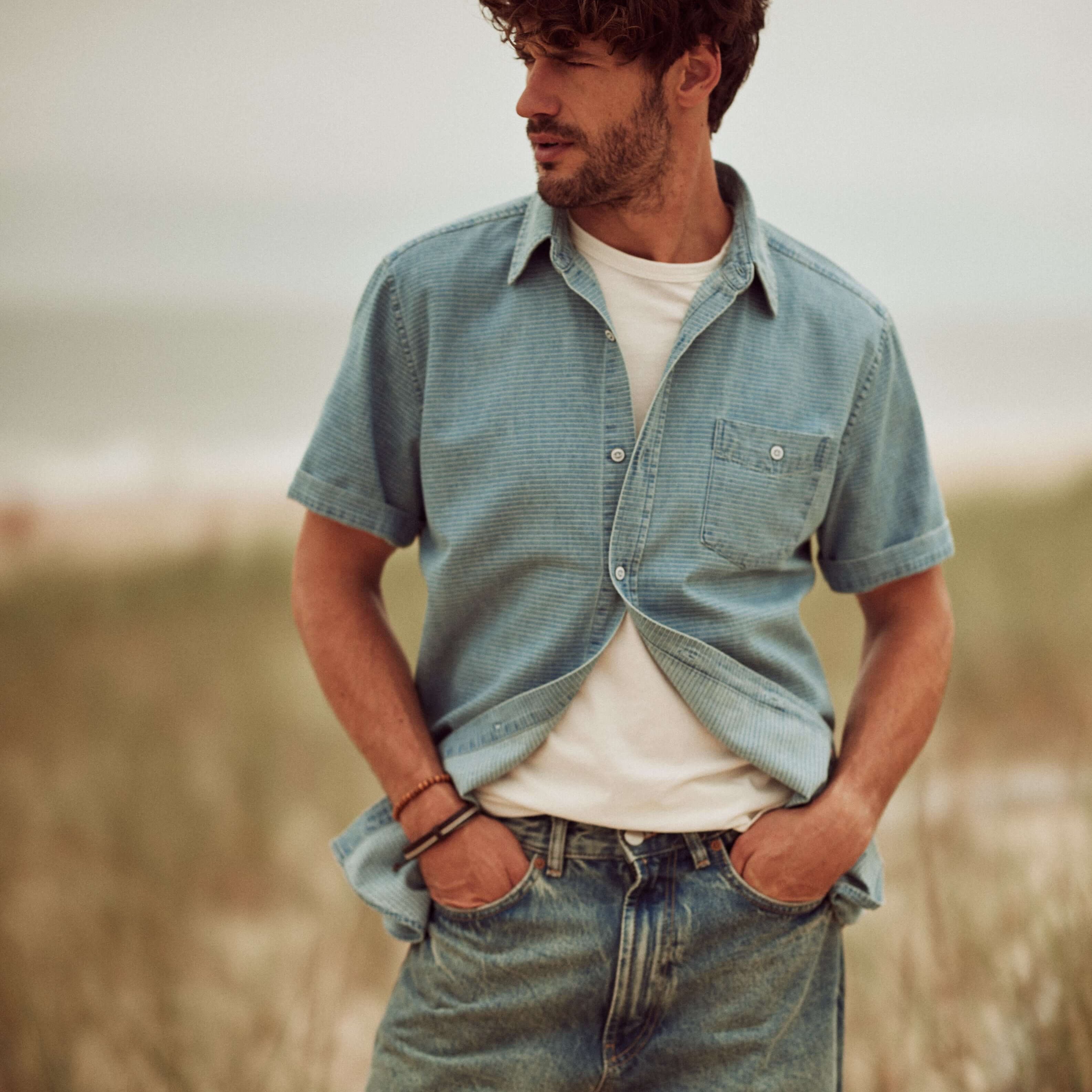 Short Sleeve Stripe Denim Shirt in Serenity Blue modeled by a man on the beach, styled with relaxed jeans.