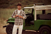 Man wearing a long sleeve burnout flannel shirt with a weathered look, standing near a vintage green jeep on the beach.