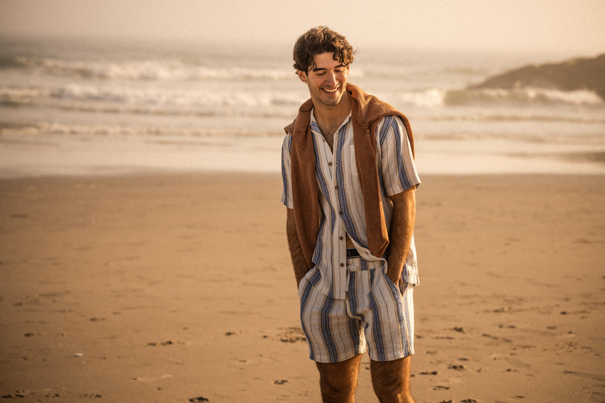 Linen Rayon Stripe Camp Shirt in Blue & White Stripe worn by man at the beach, complemented with matching shorts.