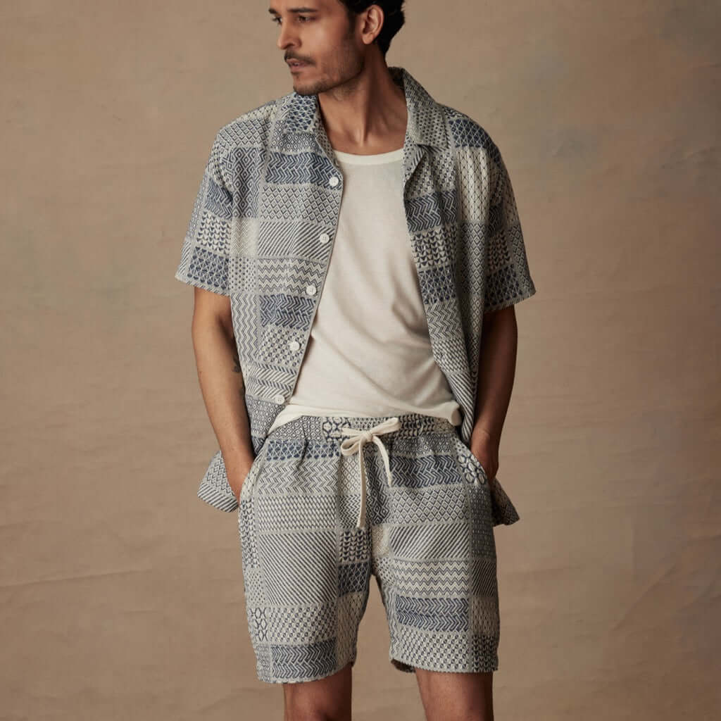 Man in a relaxed retro outfit featuring cream and navy jacquard shorts with matching top, ideal for vacation style.