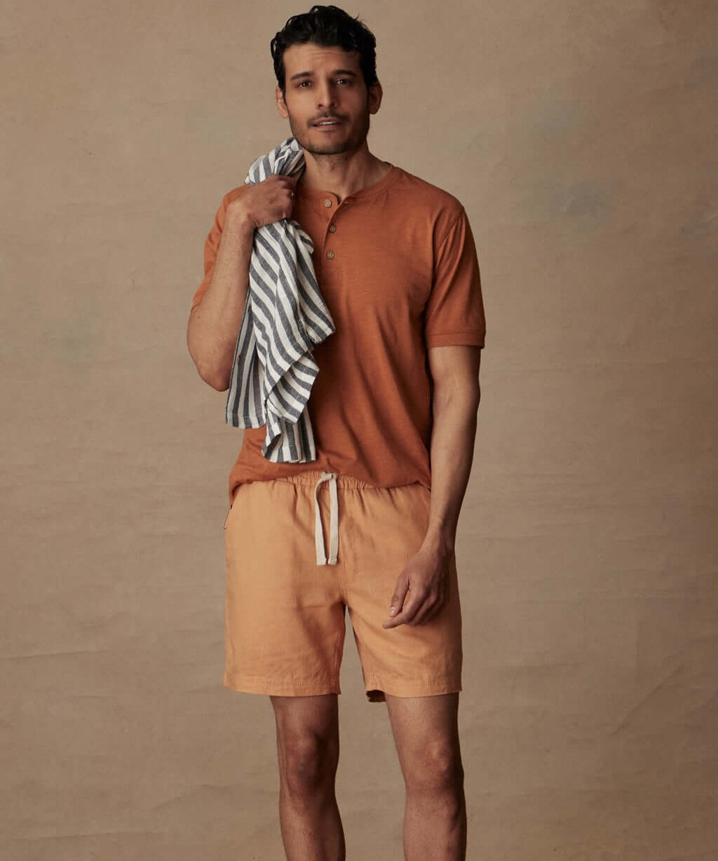 Model wearing 7" linen shorts in biscuit with a casual shirt and beach towel, perfect for warm weather outings.