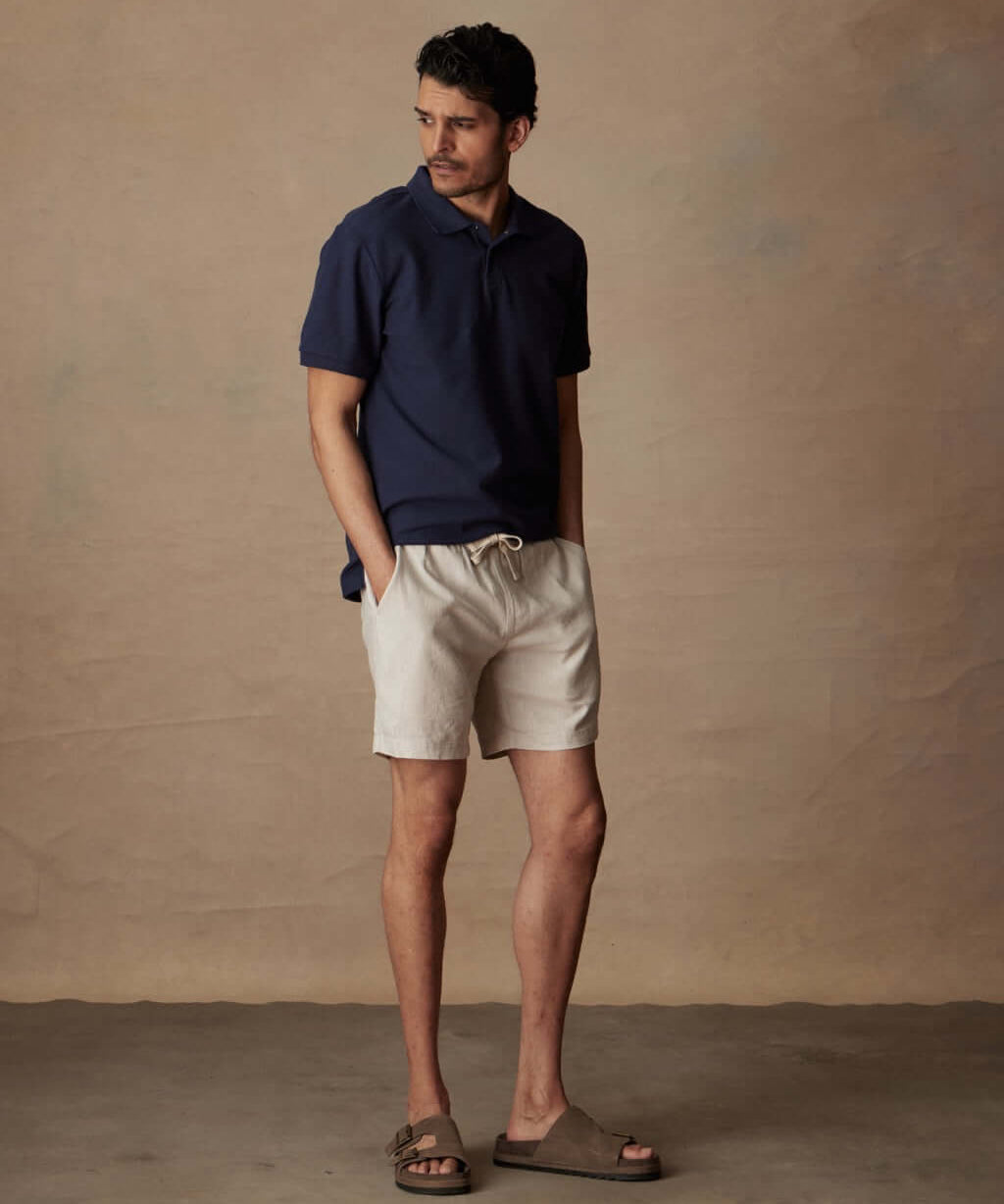 Man wearing 7" linen shorts in vapor grey and a navy polo, showcasing a relaxed summer look.