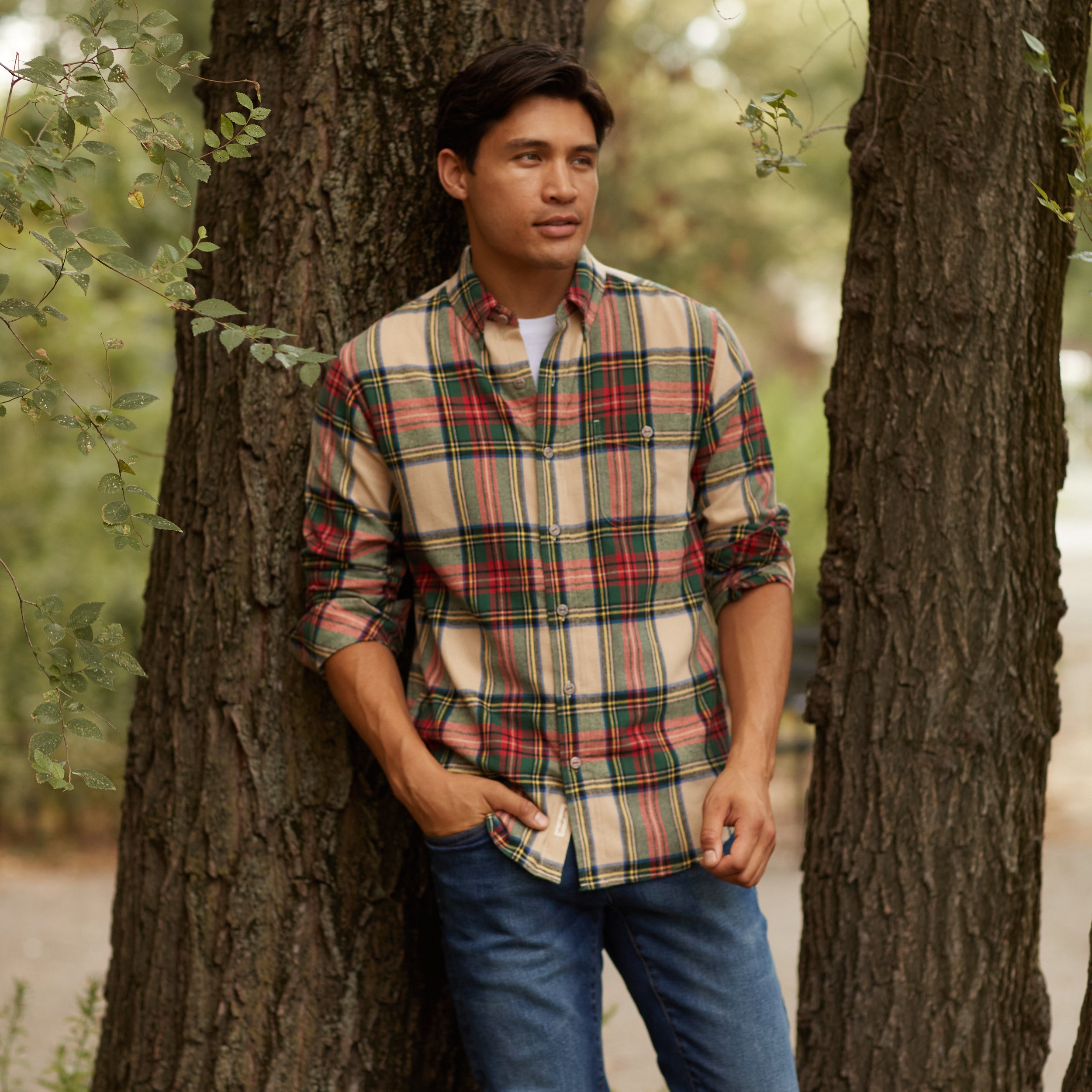 Model wearing a HOLIDAY ANTIQUE FLANNEL SHIRT in BEIGE, posed against a tree, showcasing its relaxed fit and plaid design.
