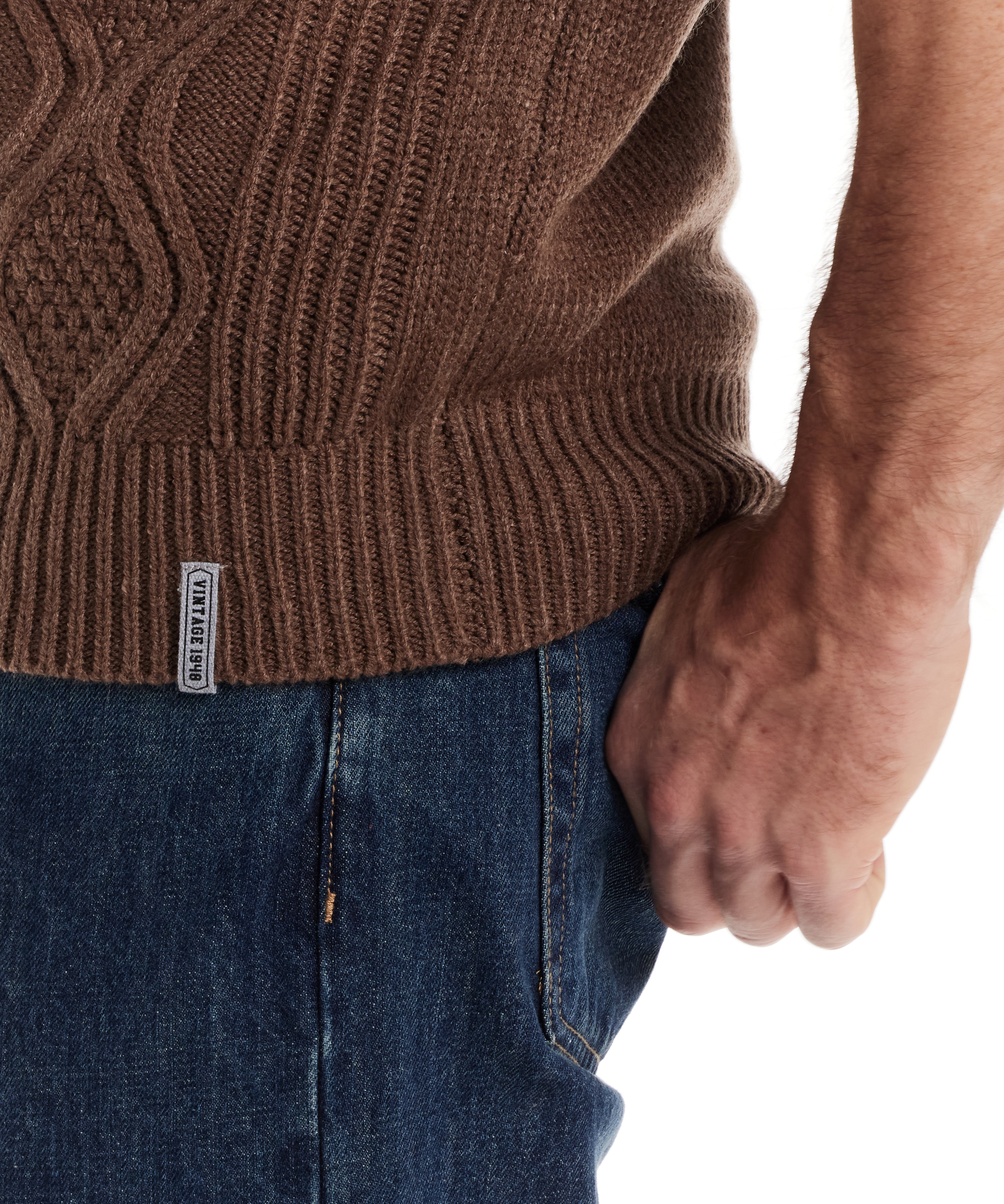 Close-up of a man's hand positioned in his pocket, showcasing the cable knit texture of a dark brown pullover.