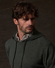 CASHMERE L/S SOLID HOODIE in FOREST GREEN worn by model against a dark background, showcasing luxury and style.