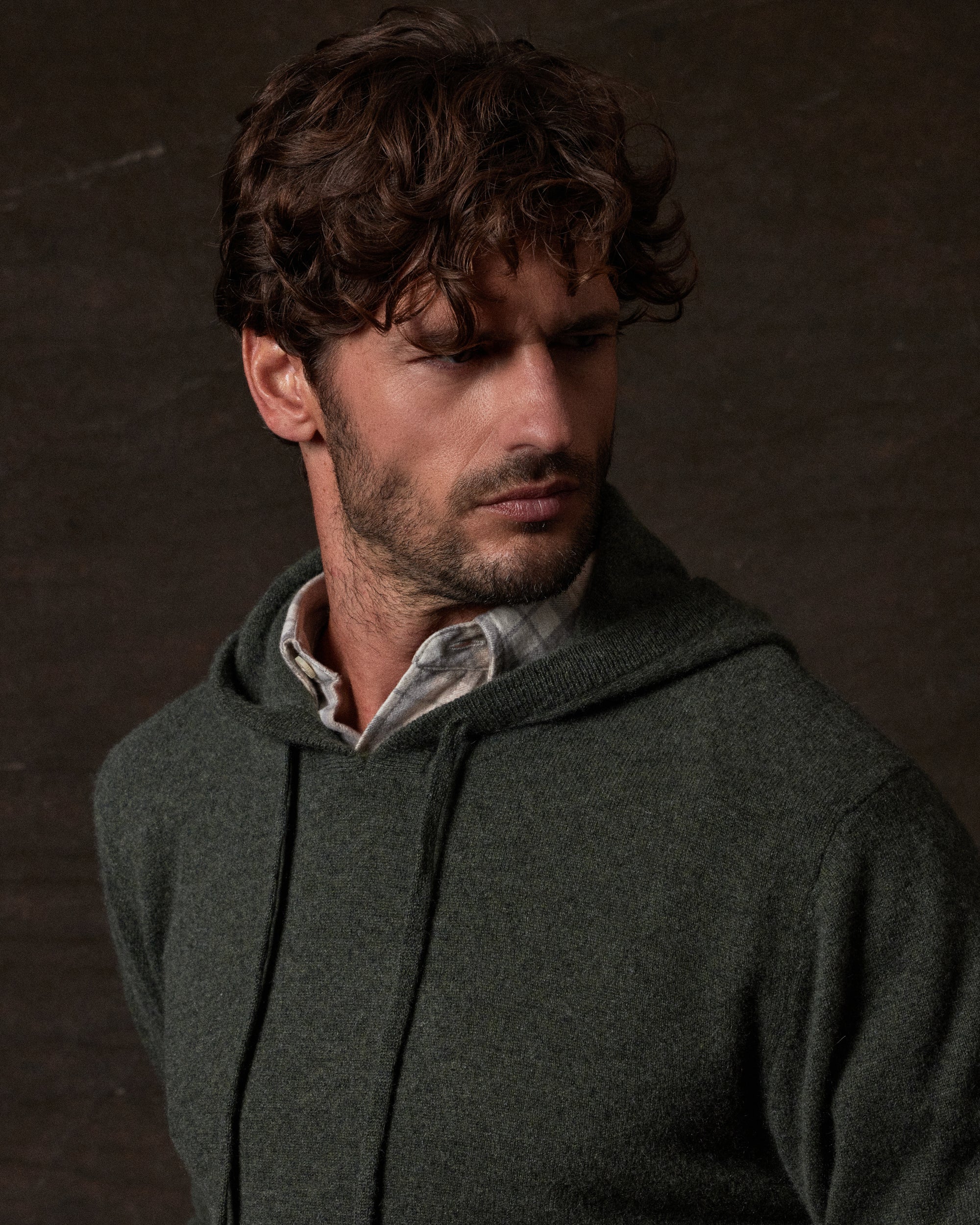 CASHMERE L/S SOLID HOODIE in FOREST GREEN worn by model against a dark background, showcasing luxury and style.