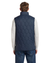 Back view of a man wearing a slate blue hexagon quilted lightweight vest over a grey sweater.