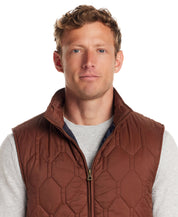Stylish man wearing a cappuccino hexagon quilted lightweight vest, showcasing its rugged charm and front zipper detail.