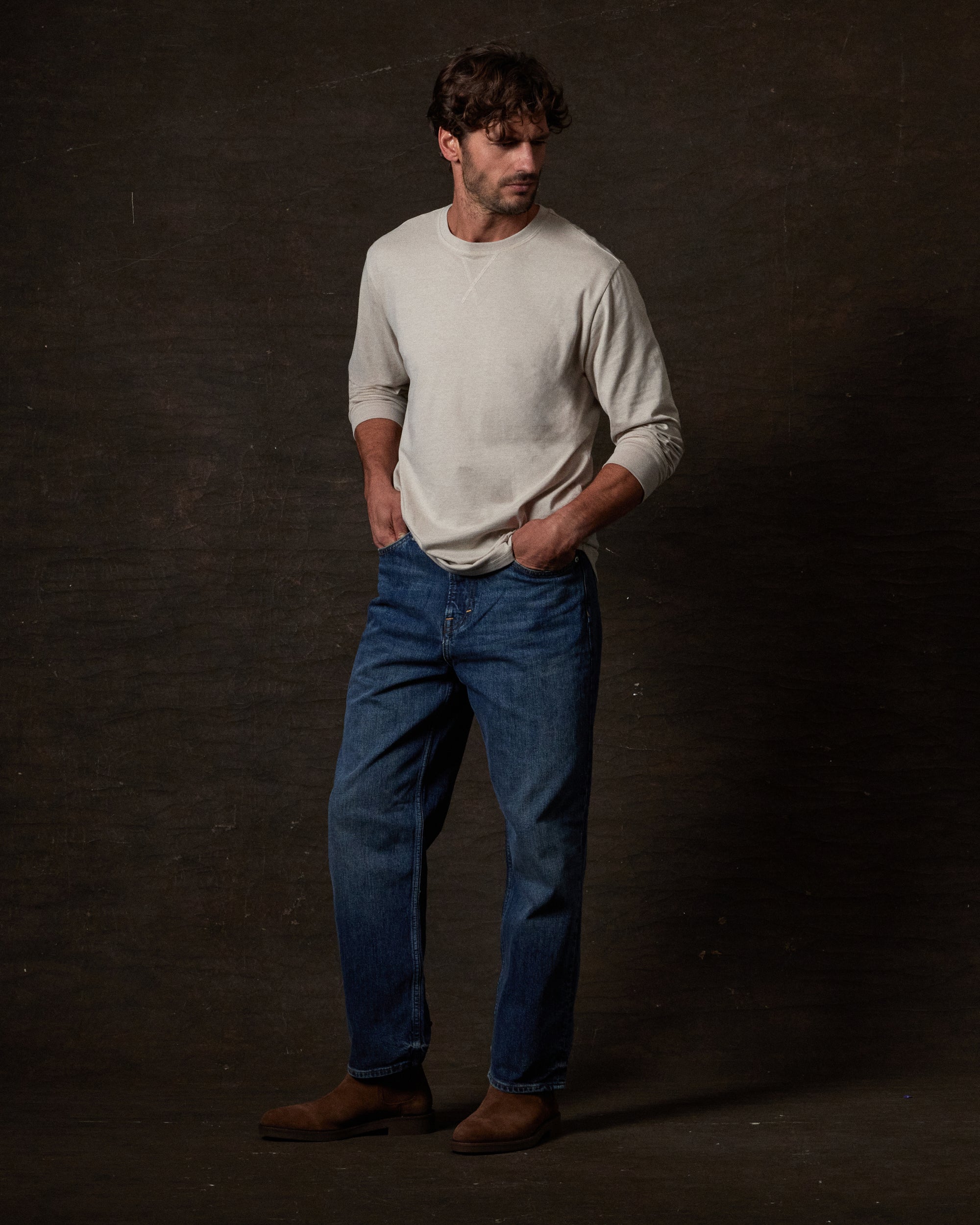 Man wearing Long Sleeve Brushed Jersey Crew in NATURAL with jeans against a dark background.