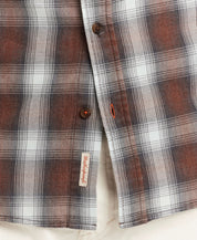 Close-up of a brown and white plaid long sleeve flannel shirt showcasing button details and a woven label.