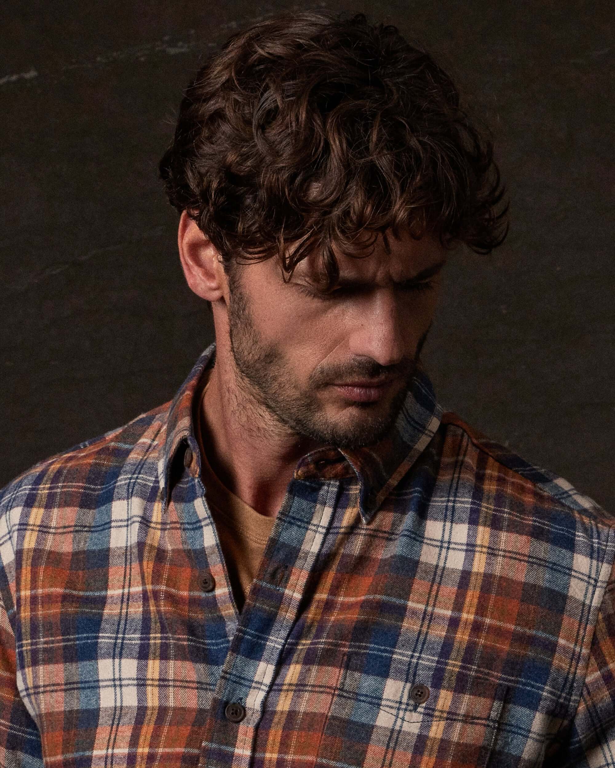 Long Sleeve Brushed Flannel in Umber worn by a model with curly hair, showcasing a rustic plaid pattern.