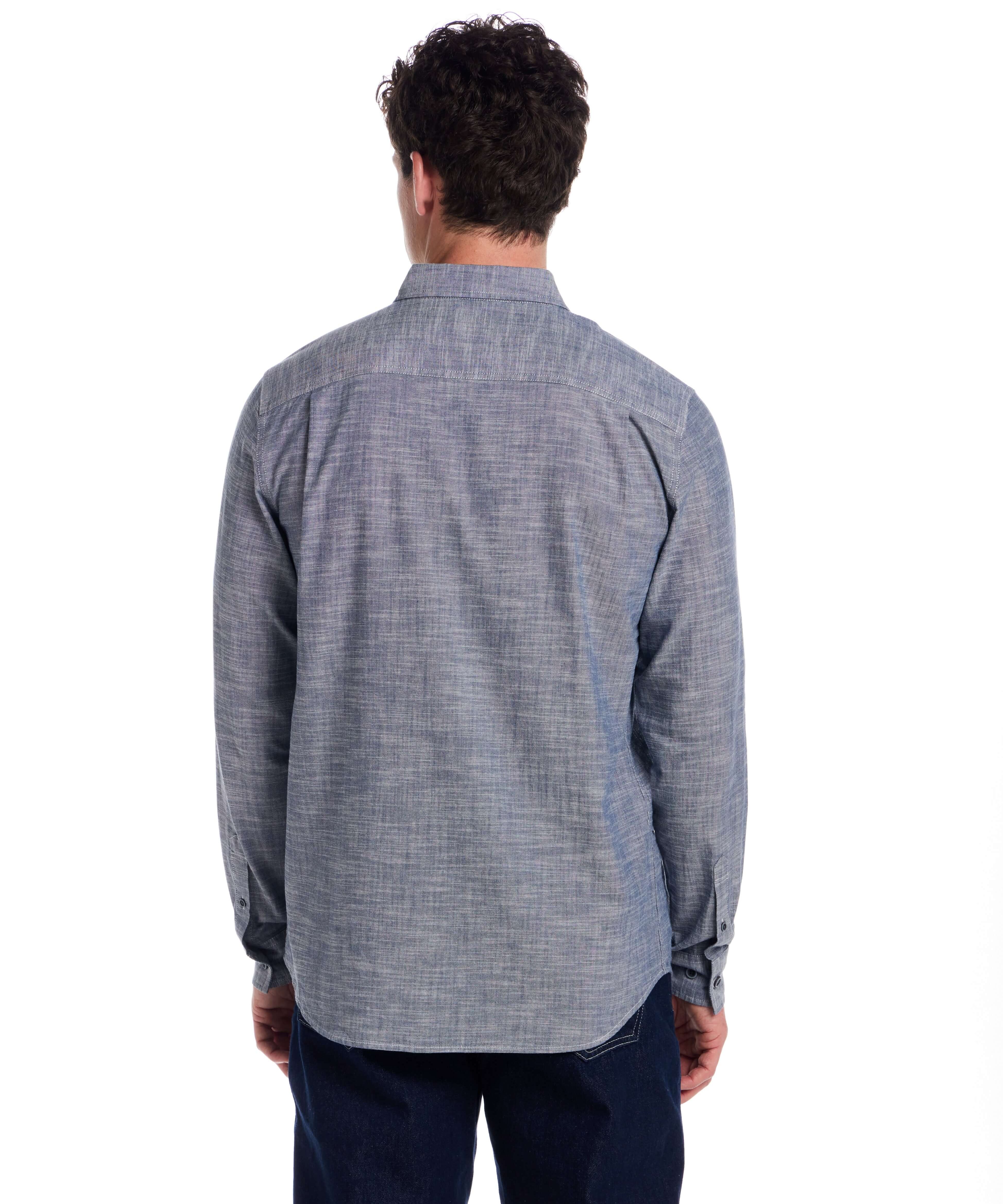 Back view of a man wearing a Long Sleeve Chambray Button-Down shirt in Insignia Blue, showcasing its classic fit and button cuffed sleeves.