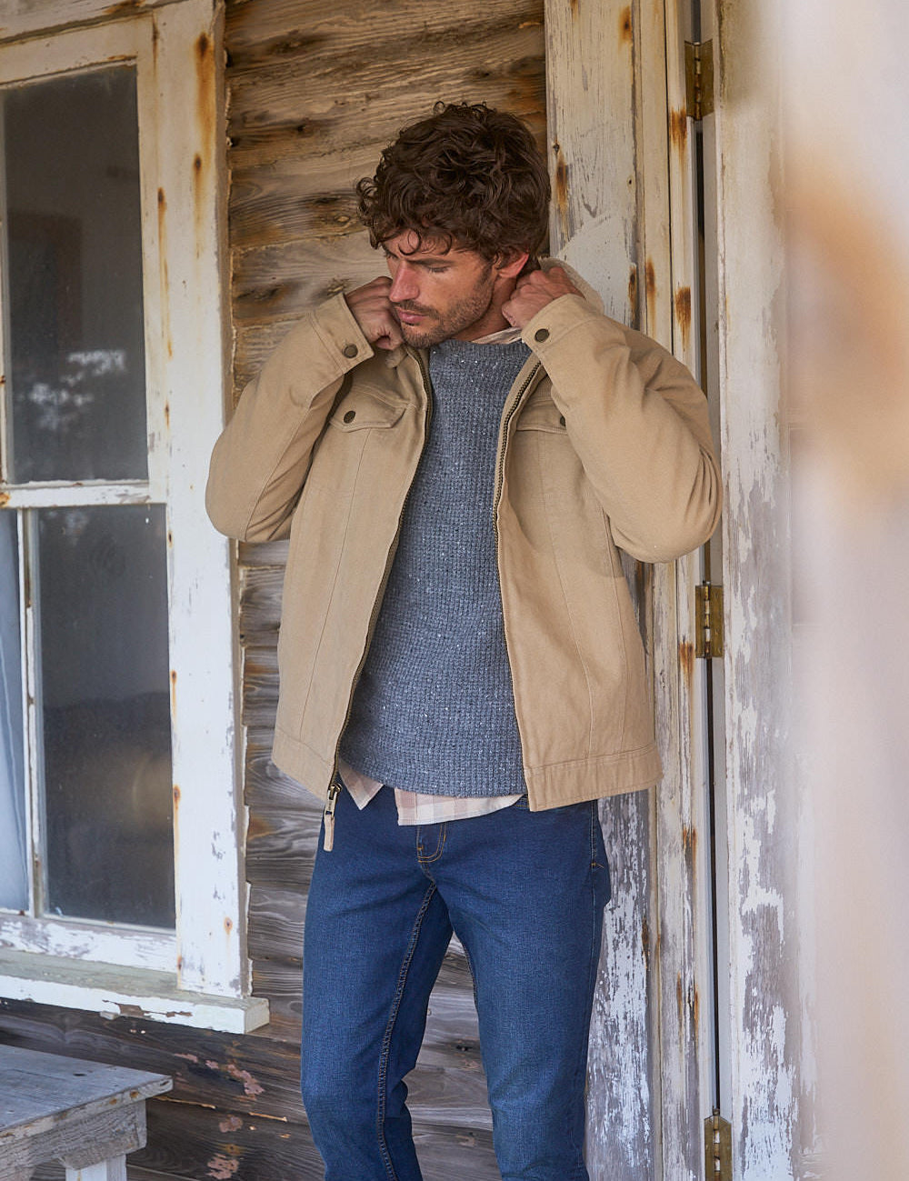 Man adjusting his Sherpa Lined Canvas Twill Trucker in White Pepper jacket in a rustic setting.