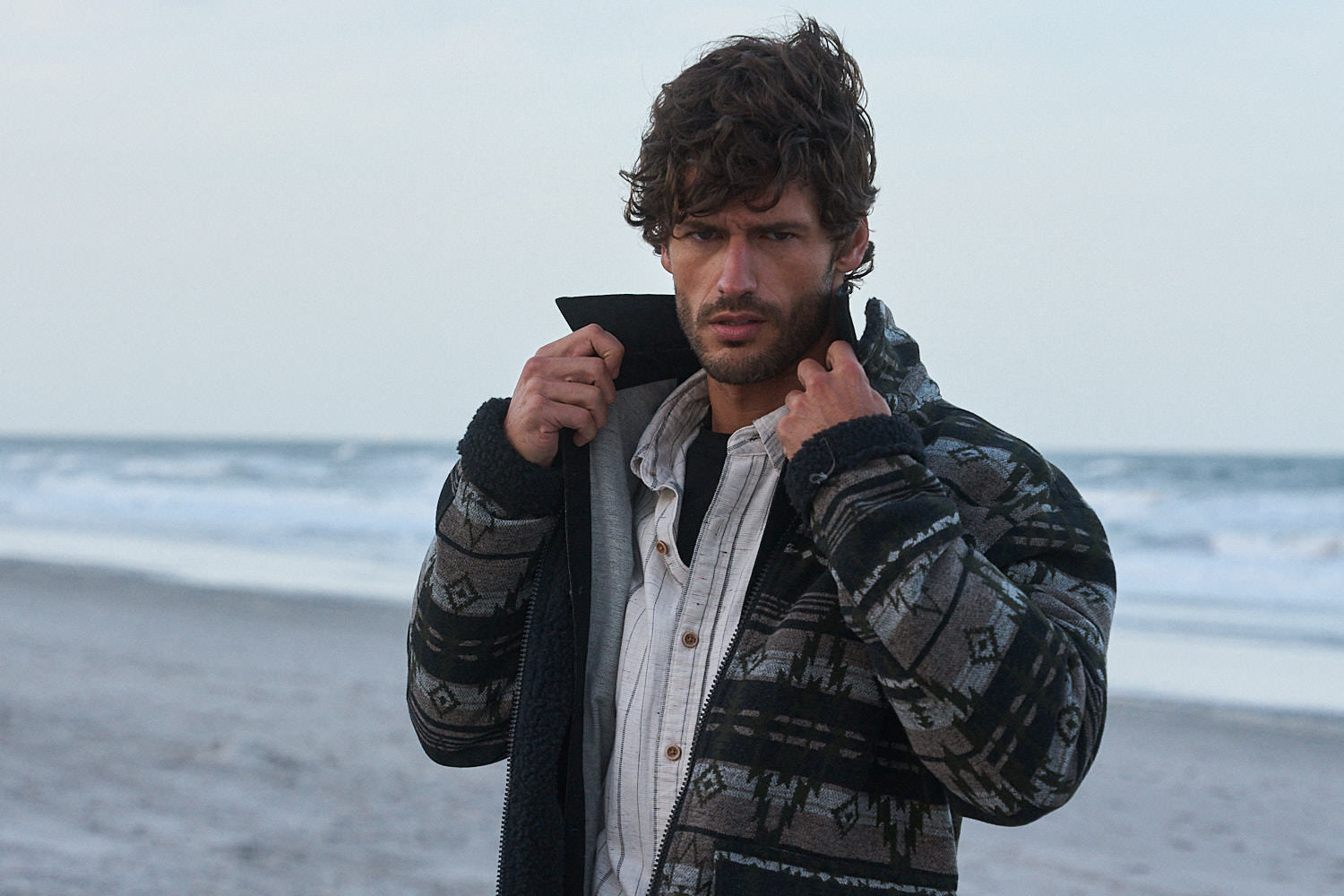 Man wearing a Berber Lined Southwest Rancher Jacket in Olive Black on the beach.