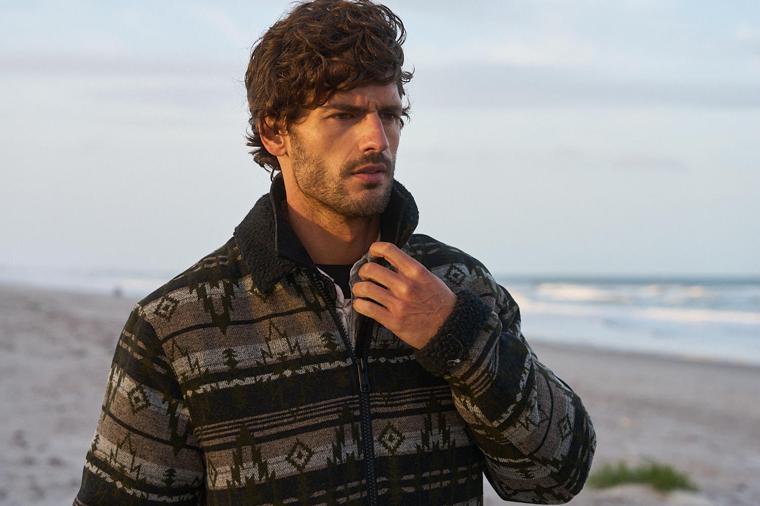 Man wearing a Berber Lined Southwest Rancher Jacket in Olive Black by the beach at sunset.