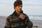 Man wearing a Berber Lined Southwest Rancher Jacket in Olive Black by the beach at sunset.
