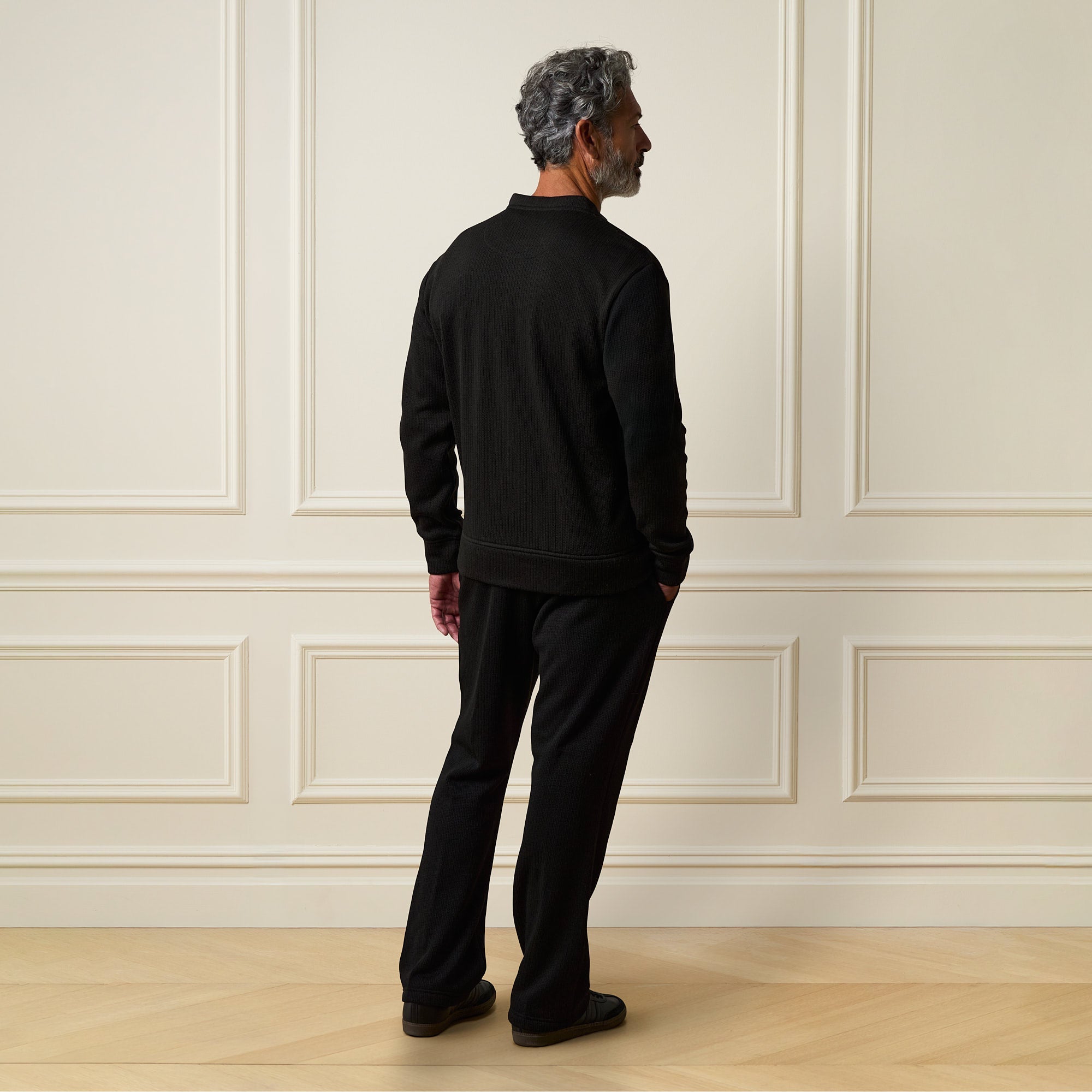 A man wearing a Ribbed Bomber Jacket in Black, showcasing the back view against a stylish interior.